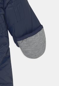 Tummansininen puhvijakki, jossa on harmaa puuvillakäsiosa ja kontrastiväri tummansinisellä trimmityöllä. Liukas pinta, jossa näkyvät saumat ja ompeluyksityiskohdat.