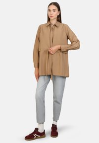 Beige long-sleeve shirt with collar, tied at the waist, paired with light blue jeans and burgundy sneakers. Simple, smooth texture.