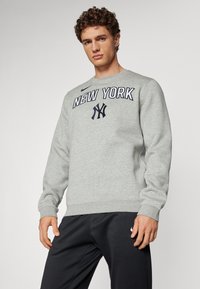 Grå hettegenser med "NEW YORK" og NY-logo i marineblå trykk. Har rund hals og ribbestrikkede ermer. Kombinert med mørke bukser.