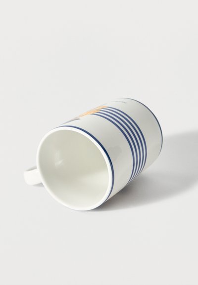 Fehér kerámia bögre kék vízszintes csíkokkal és virágos mintával, fekve egy fehér felületen.