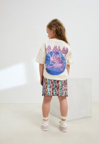 Lichtbeige T-shirt met een blauwe en roze luipaardprint op de achterkant, gecombineerd met een meerkleurige paillettenrok met golvende patronen.