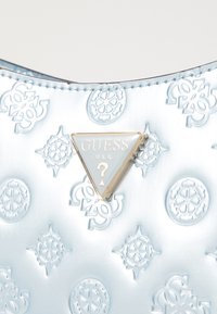 Lyseblå præget håndtaske med et trekantet guld Guess-logo, intrikat mønstret tekstur og glat læderfinish.