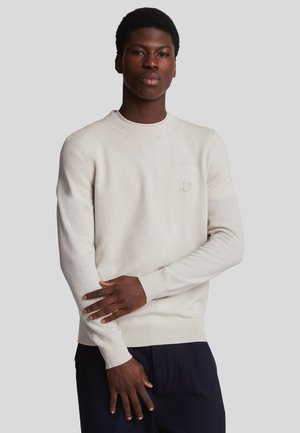 Maglione beige chiaro realizzato in tessuto morbido, con scollatura e polsini a coste, con un piccolo logo ricamato sul lato sinistro del petto.