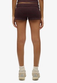 Donker gestreepte shorts met een aansluitend ontwerp, voorzien van een gladde textuur en een elastische tailleband, gecombineerd met lichtgekleurde enkelkousen en sneakers.