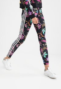 Svarta leggings med ett livligt blommönster i rosa, grönt och lila, med vita ränder längs sidorna och en figurnära design.