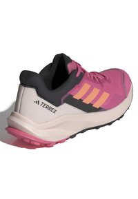 Zapatilla deportiva rosa y negra con un upper texturizado, tres franjas naranjas y una suela acolchada. Logotipo notable y acentos de color visibles.