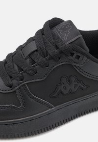 Svart sneaker med en slät syntetisk ovandel, texturerade tygdetaljer, snörning och en logo broderad på sidan. Gummisula.