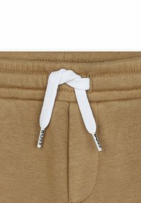 Pantaloni della tuta in cotone color beige con cordino bianco e un'etichetta con la scritta "BOSS". Tessuto testurizzato e dettagli dell'elastico in vita.
