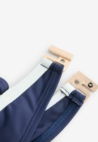 Tkanina na plavky v námorníckej modrej a bielej farbe so zapínaním na zlatý kovový klip na bielom pozadí.