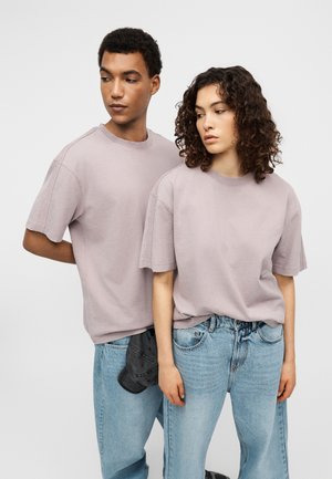 Φαρδιά μπλουζάκια σε ανοιχτό μωβ χρώμα από απαλό βαμβάκι, με κοντά μανίκια και χαλαρή εφαρμογή, συνδυασμένα με ανοιχτό μπλε φαρδιά τζιν.