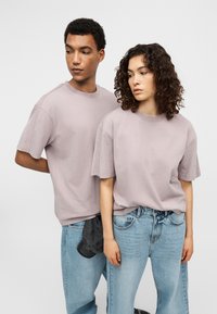 Φαρδιά μπλουζάκια σε ανοιχτό μωβ χρώμα από απαλό βαμβάκι, με κοντά μανίκια και χαλαρή εφαρμογή, συνδυασμένα με ανοιχτό μπλε φαρδιά τζιν.