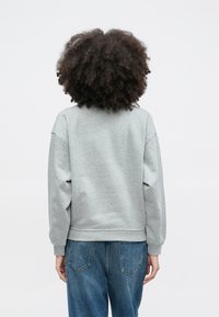 Pelēks džemperis ar vaļīgu piegriezumu, ribota apmale un maliņa, gluda tekstūra. Kombinēts ar zilām džinsa biksēm.