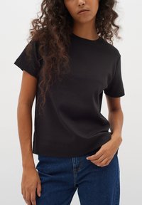 T-shirt noir à manches courtes en tissu doux avec un col rond et une coupe décontractée, associé à un jean en denim bleu.