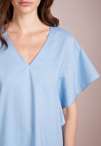 Blusa azzurra chiara con scollatura a V e maniche a farfalla, realizzata in tessuto morbido con una vestibilità rilassata e una leggera lucentezza. Dettagli di design minimalisti.