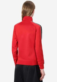 Giacca sportiva rossa con colletto alto, strisce laterali nere e texture liscia. Caratterizzata da maniche lunghe e design aderente.