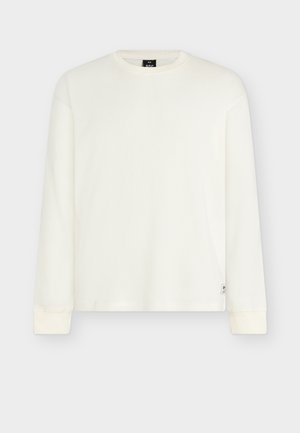 Weißes, geripptes Langarmshirt mit Rundhalsausschnitt und enganliegenden Bündchen. Verfügt über ein kleines Logoetikett auf der unteren linken Seite. Weiche Textur.