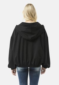 Zwarte cropped hoodie met een capuchon met trekkoord, brede mouwen en een elastische zoom en manchetten. Gecombineerd met blauwe spijkerbroeken.