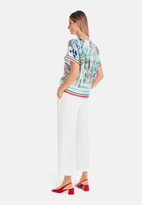 Locker sitzende, kurzärmlige Bluse in Hellblau mit Blumen- und geometrischen Mustern; kombiniert mit weißen Culottes und roten High Heels.