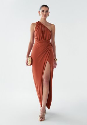 Ühe õla kleit, roostepunane, valmistatud siledast kangast, drapeeritud disainiga, kõrge lõhiku ja vöökohale seotud detailiga. Kuldne klambri ja sandaalid.