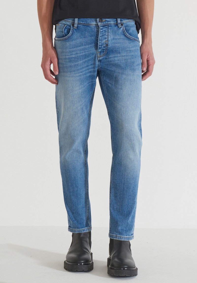 Jeans de denim azul claro con un corte recto, cinco bolsillos, un desvanecimiento sutil y costuras en contraste, combinados con botas negras hasta el tobillo.