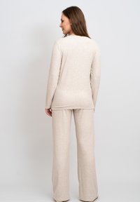 Beige stickad lounge set bestående av en långärmad topp och byxor med vida ben. Mjuk textur med avslappnad passform. Minimalistisk design, utan mönster eller detaljer.