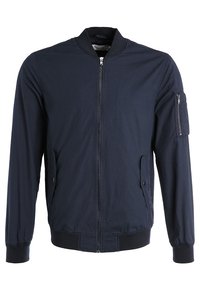 Marinblå bomberjacka med dragkedja fram, två sidofickor och en ficka med dragkedja på ärmen. Ribbad mudd och nederkant, tillverkad av lättviktig material.