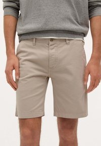 Pantalones cortos de algodón beige con un corte recto, que presentan un frente plano, dos bolsillos laterales y un cierre de botón único en la cintura.