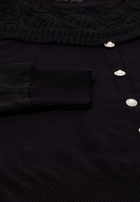 Cardigan nero con un design floreale a trama lungo il colletto, polsini a costine e decorativi bottoni simili a perle.