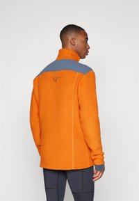 Orange fleece jacket with a grey shoulder panel. Features a high collar and textured fabric. Embroidered logo on the back.