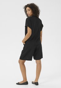 Schwarzes Leinen-T-Shirt mit kurzen �Ärmeln und lockerer Passform, kombiniert mit passenden schwarzen Shorts. Weicher Stoff, Taschen an den Shorts und schlichtes Design.