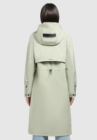 Light green waterproof coat with a hood, featuring a cinched waist, flap design, and black logo accents on the back and sleeves.