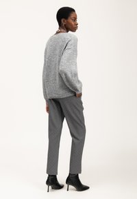 Maglione grigio a maglia con maniche lunghe abbinato a pantaloni slim-fit grigi con pois bianchi. Stivaletti neri alla caviglia completano l'outfit.