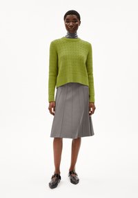 Groene gebreide trui met een textuurpatroon, gecombineerd met een grijze A-lijn rok met verticale naden en zwarte instap schoenen.
