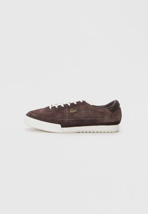 Zapatillas bajas de ante marrón con suela y cordones blancos, que presentan un pequeño logotipo de cocodrilo dorado en el lateral.