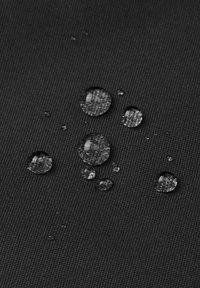 Waterdruppels op gestructureerde zwarte stof, die een glad oppervlak tonen met variërende groottes van duidelijke bolletjes die licht weerkaatsen.
