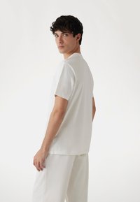 Camiseta blanca de manga corta en una tela suave y lisa, con un cuello redondo clásico y un corte relajado. Diseño liso, sin patrones adicionales.