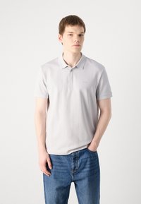 Polo shirt gris clair avec un col replié, une patte de boutonnage et des rayures verticales subtiles. Associé à un jean en denim bleu.