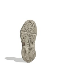Sole of a beige sneaker with textured circular and linear patterns, casting a shadow on a white background.