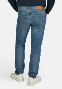 Blauwe denim jeans met een rechte snit, voorzien van achterzakken, subtiele stiksels en een leren patch op de tailleband. Draagt men met witte sneakers.