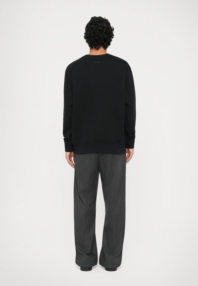 Sort sweatshirt med ribbede mansjetter og kant, vist fra ryggen med grå bukser. Simpelt design, blød tekstur, ingen synlige mønstre.