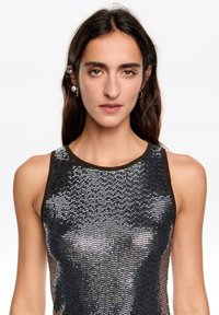 Bezrekawnik z czarno-srebrnym wzorem cekinów i brązową lamówką. Cekiny tworzą teksturowaną, połyskującą powierzchnię.