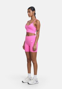 Rosa sportig crop-top och matchande shorts i en åtsittande design. Tillverkad av texturerat tyg, med en liten logotyp på toppen. Vita sneakers ingår.