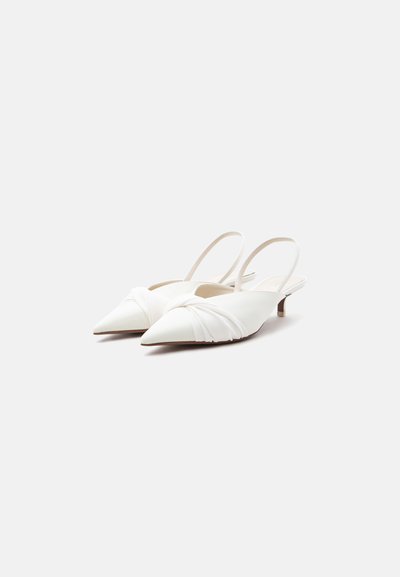 Άσπρα μυτερά slingback παπούτσια με χαμηλό τακούνι και στριφτό ύφασμα μπροστά, σε απλό ανοιχτό φόντο.