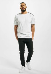 White short-sleeve t-shirt with black shoulder accents, paired with black slim-fit pants and white sneakers, standing against a plain background.