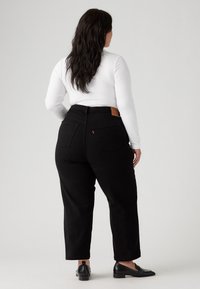 Vaqueros negros de cintura alta con un diseño de pierna recta, detalles de bolsillos traseros de parche y una etiqueta de cuero marrón con marca en la cinturilla.