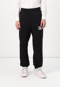 Zwarte sweatpants met elastische tailleband, voorzien van een vierkante logopatch. Gemaakt van zachte stof, met een taps toelopend design en boorden bij de enkels.