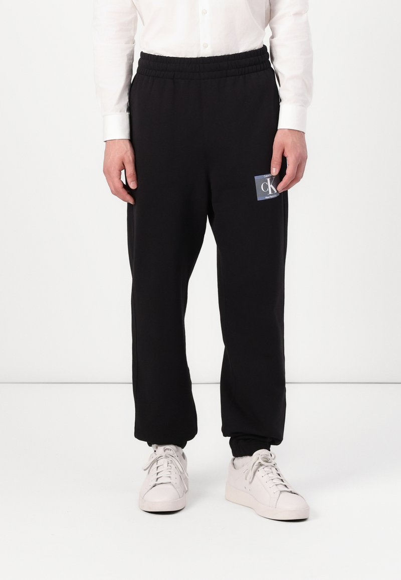 Zwarte sweatpants met elastische tailleband, voorzien van een vierkante logopatch. Gemaakt van zachte stof, met een taps toelopend design en boorden bij de enkels.