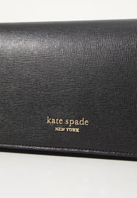 Svart, teksturert skinnlommebok med en glatt overflate, med gull "kate spade NEW YORK" logo. Kompakt, rektangulært design uten tilleggsdekorasjoner.