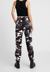 Haut court noir côtelé associé à un pantalon camouflage taille haute avec poches élastiquées, présentant des motifs gris, noir et bordeaux. Bottes noires épaisses.