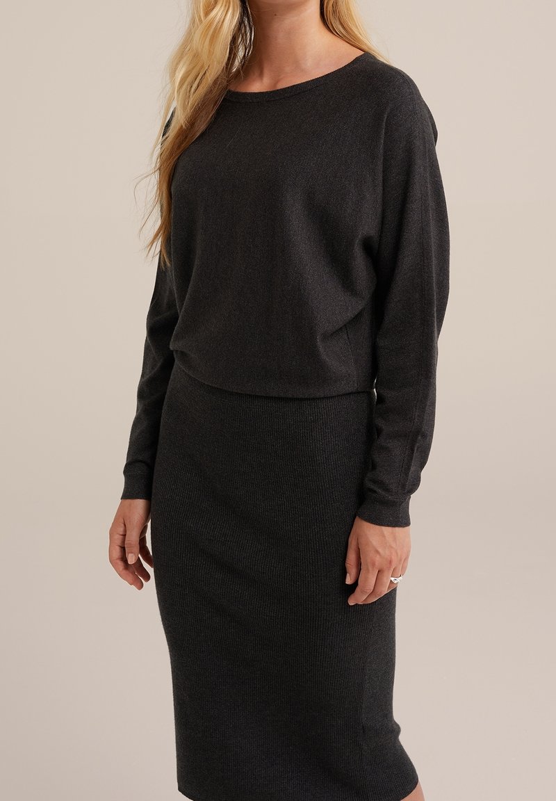 Pull cropped à manches longues gris foncé associé à une jupe midi ajustée à côtes dans une couleur assortie. Texture lisse et design minimaliste.